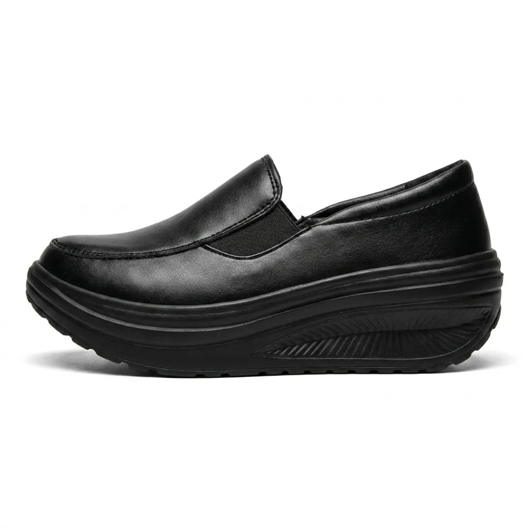 Black faux-leather slip-on shoe in side profile, showing the elastic panel and curved wedge sole 1