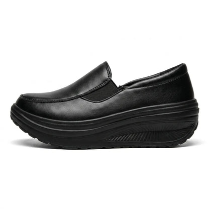 Black faux-leather slip-on shoe in side profile, showing the elastic panel and curved wedge sole 1