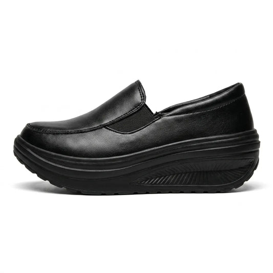 Black faux-leather slip-on shoe in side profile, showing the elastic panel and curved wedge sole 1