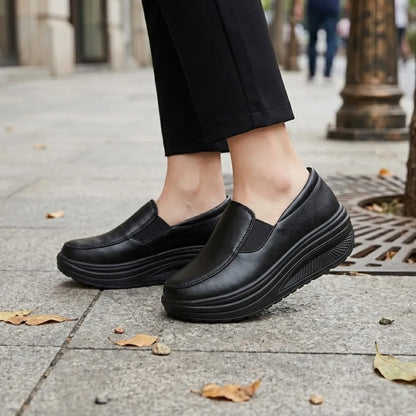 Black slip-on shoes worn by a woman in dark trousers on a paved street 2