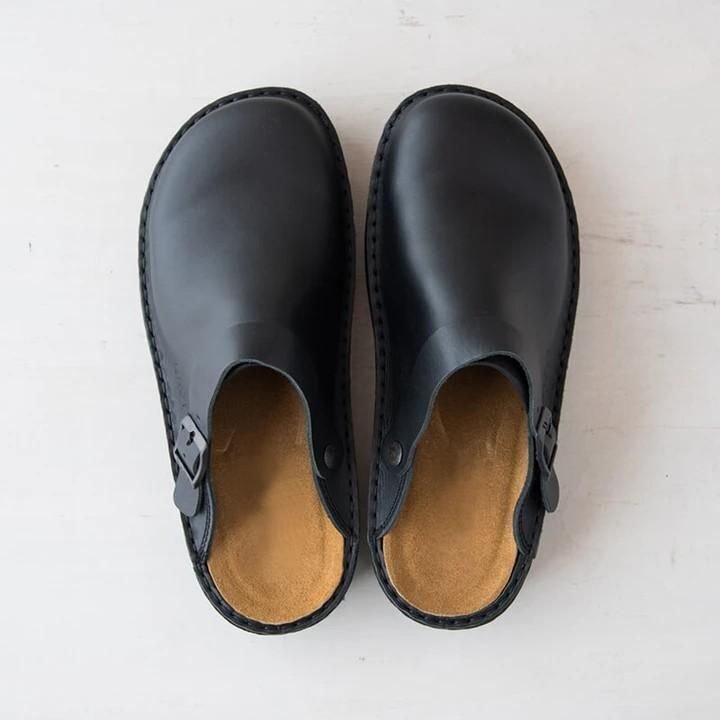 Top-down view of black leather mule clogs with visible stitching, side buckle and a tan cushioned footbed. 3