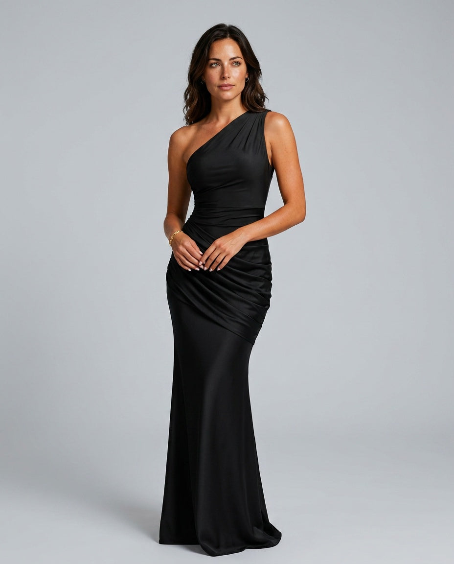 Model in the black satin maxi dress, front view, one shoulder with ruched draping across the hip, hands clasped. 1