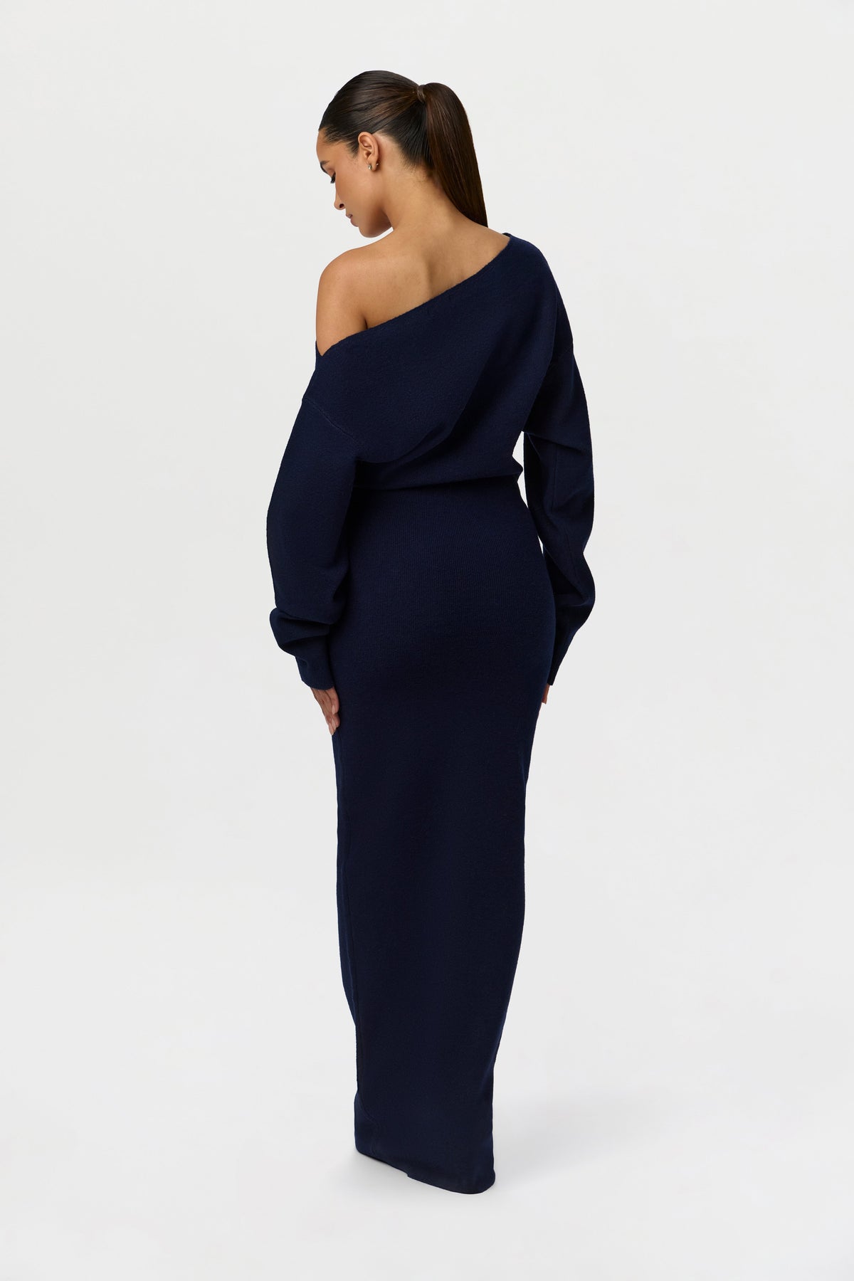 Back view of the navy knit maxi dress, with the model looking down to show the slanted neckline and fitted skirt. 26
