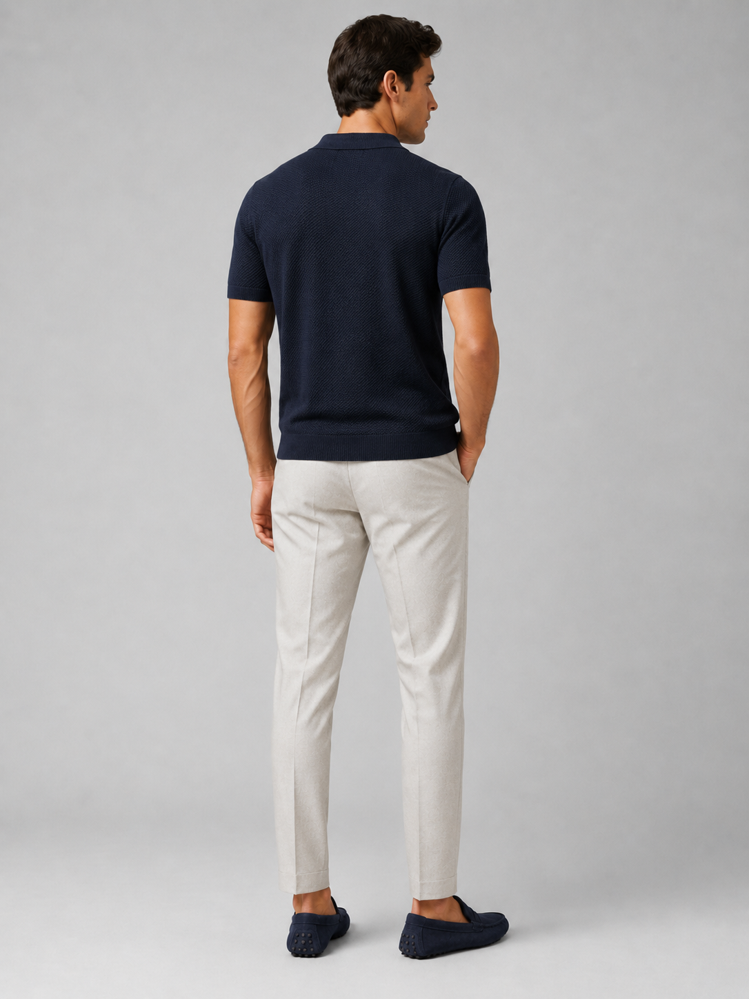 Back view of navy knit polo on model, with light grey trousers and navy suede loafers 38