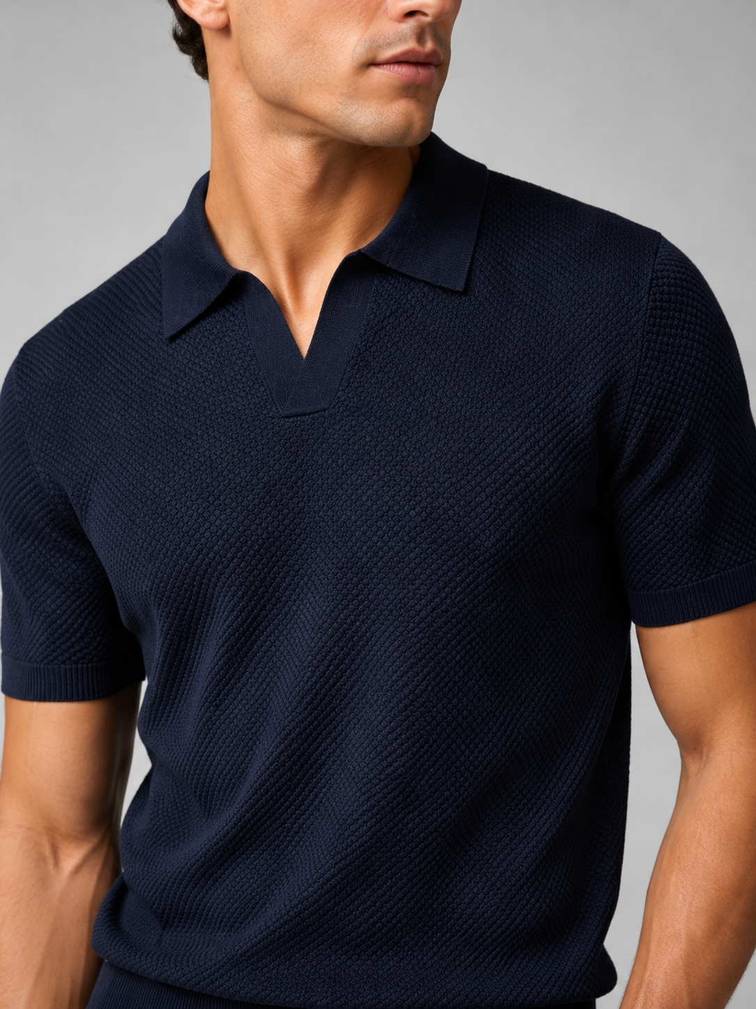 Close-up of navy knit polo showing the textured honeycomb stitch, open V-neck collar and ribbed sleeve cuff 36