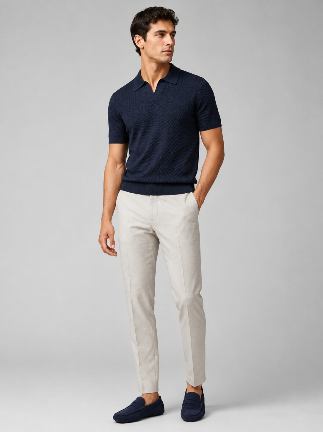 Full-length studio view of model in navy knit polo, light grey trousers and navy suede driving loafers 37