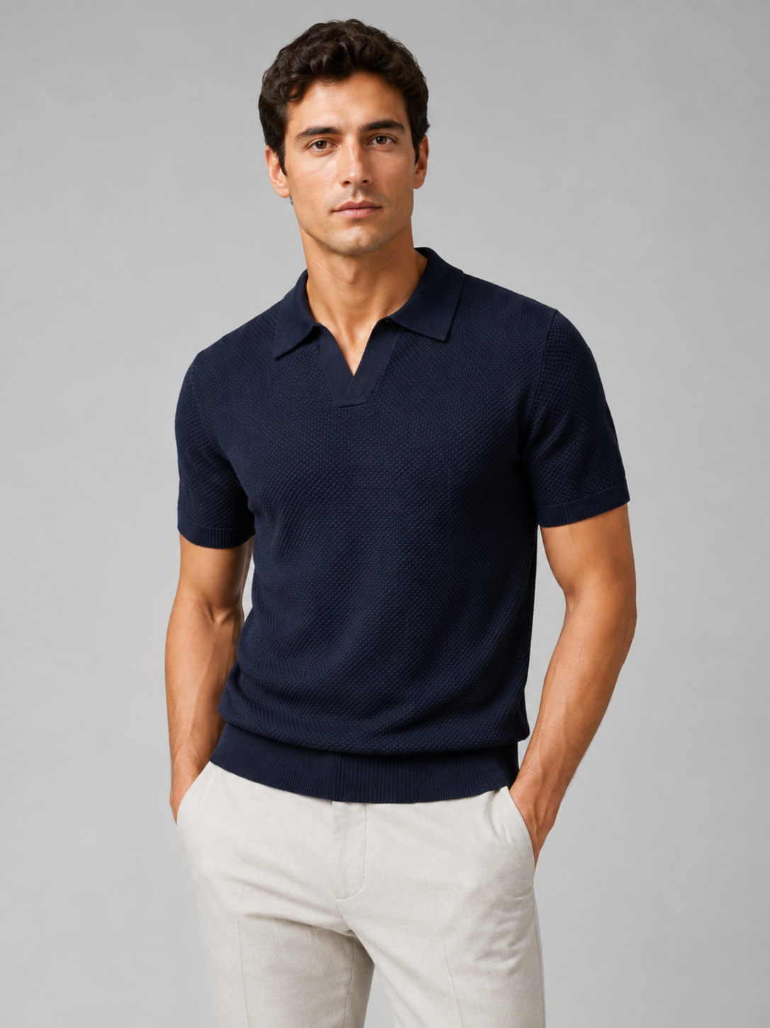 Model wearing navy textured knit polo with open V-neck collar, hands in pockets, light grey trousers, studio shot 35