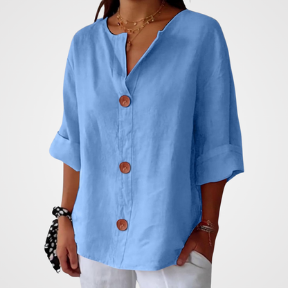 Light blue loose blouse worn by a model against a plain pale background, showing the V-neckline, three buttons and relaxed sleeves. 14