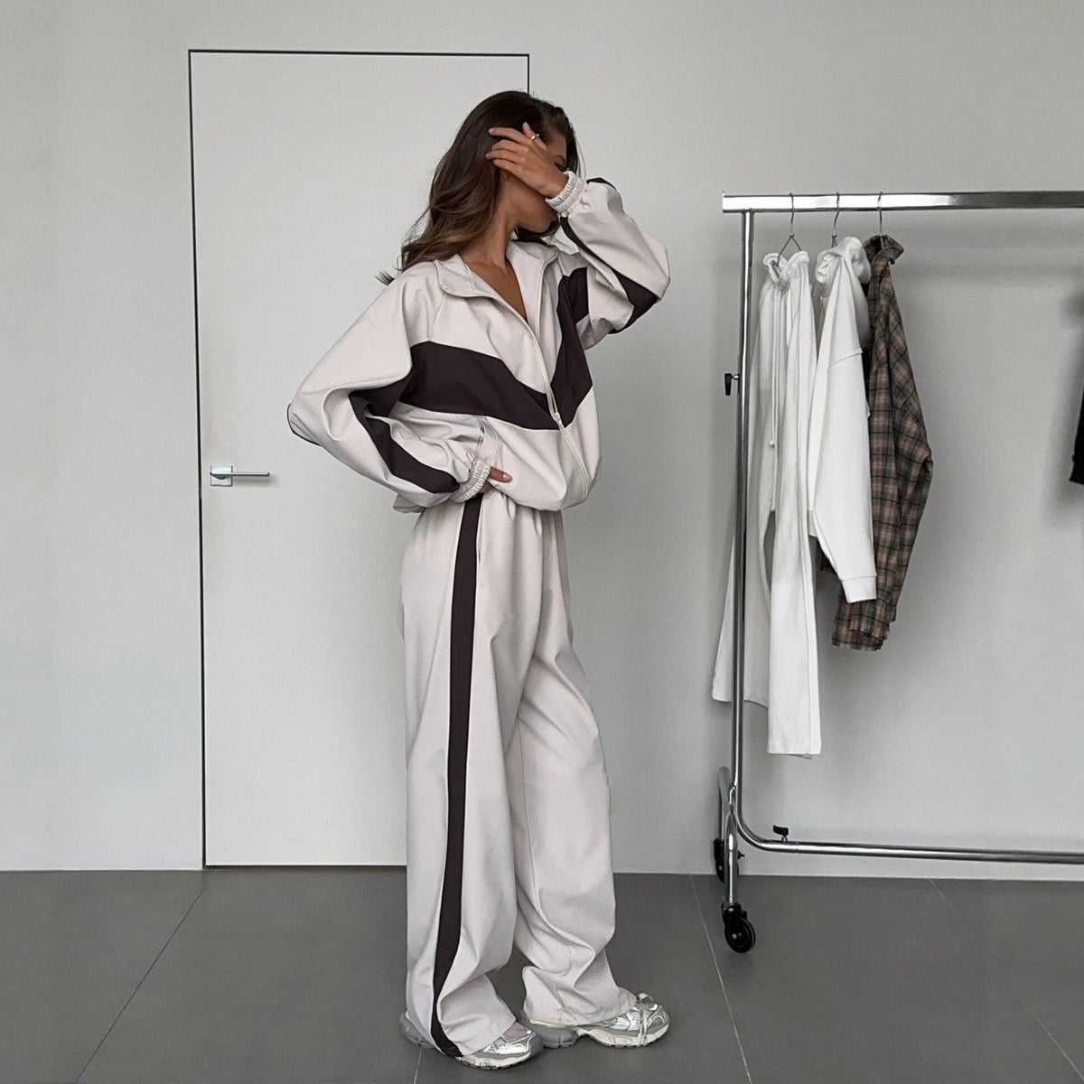 Side view of a model in a cream tracksuit with dark brown chevron panels on the jacket and stripes down the trousers. 3