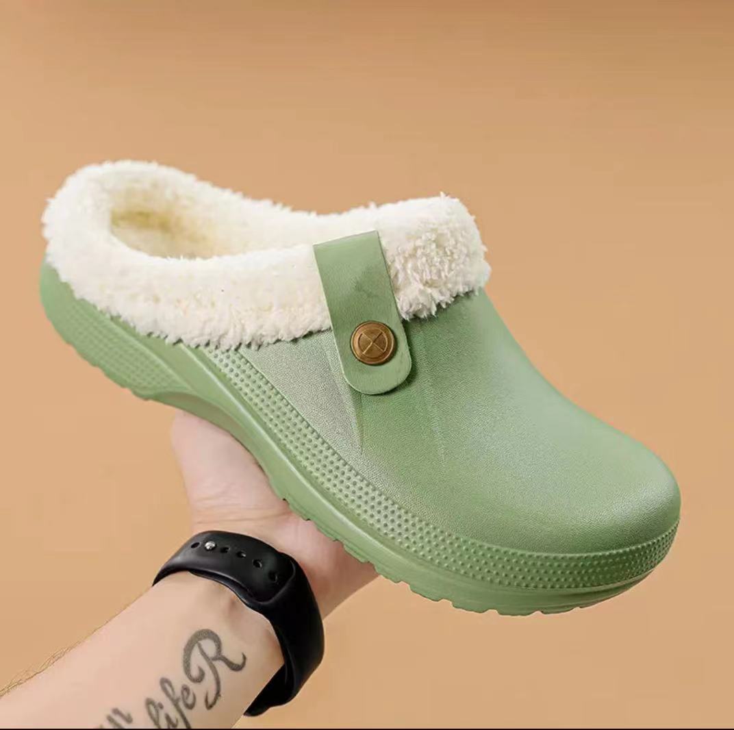Hand holding a light green clog with cream fleece lining and a matching buttoned strap 13
