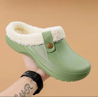 Hand holding a light green clog with cream fleece lining and a matching buttoned strap 13