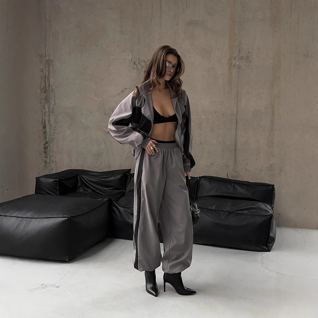 Model in a grey jacket with dark panels and baggy grey trousers, styled with a black bralette and heeled boots in a concrete room. 7