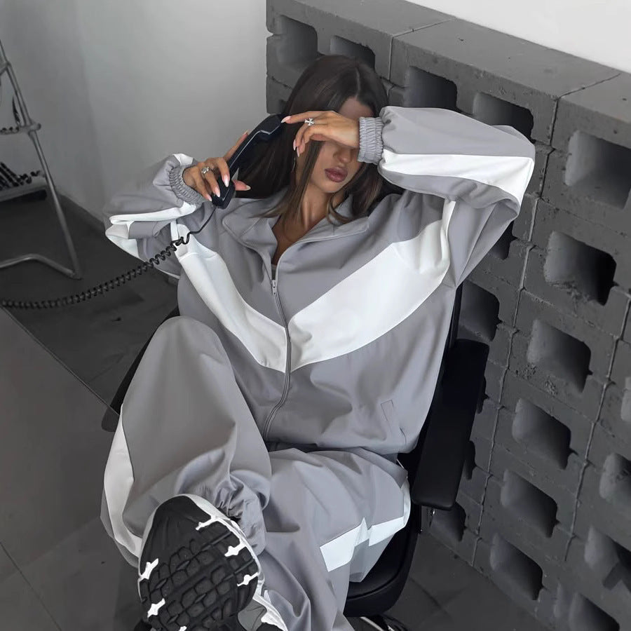 Model in a grey and white chevron-panelled zip jacket and matching trousers, seated in a chair holding a corded telephone. 1