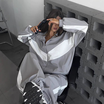 Model in a grey and white chevron-panelled zip jacket and matching trousers, seated in a chair holding a corded telephone. 1