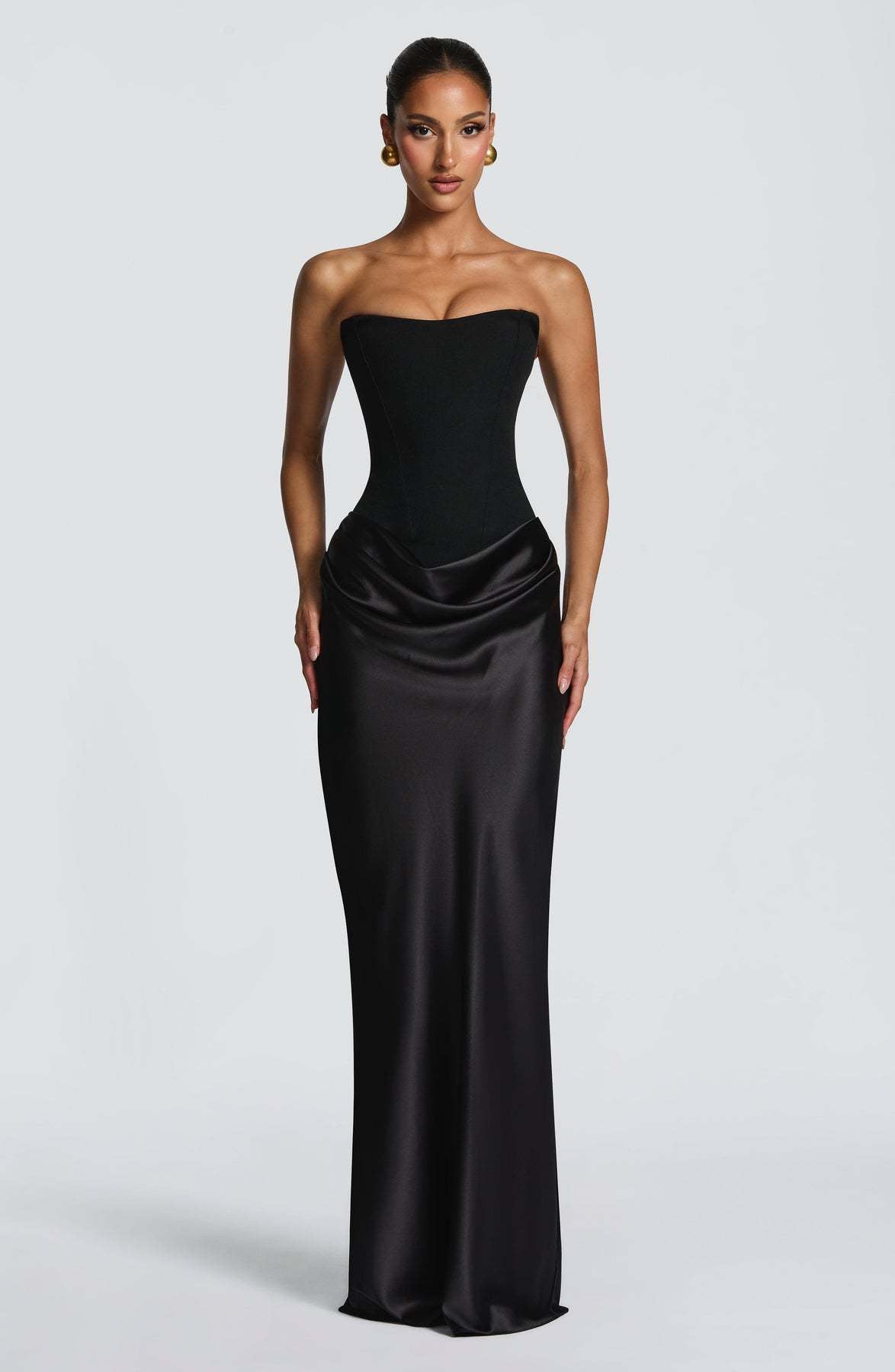 Model wears the black strapless corset dress, front view, with draped satin hip detail and gold earrings 21