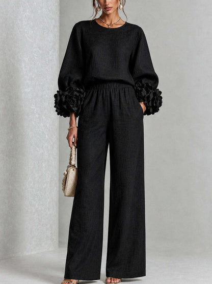 Model standing front-on in the black version, with fabric flowers at the cuffs and a cream handbag 2