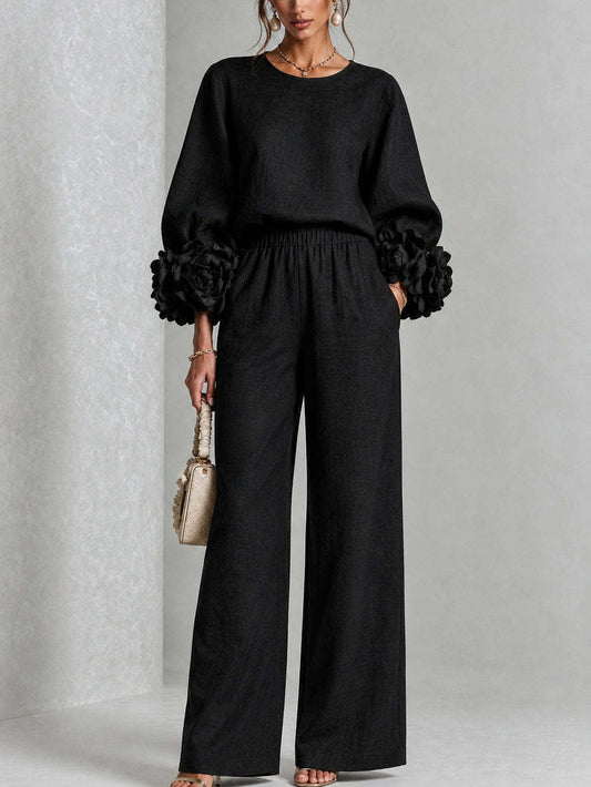 Model standing front-on in the black version, with fabric flowers at the cuffs and a cream handbag 2