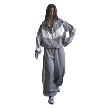 Model walking in a grey tracksuit set with white chevron panels on the jacket and elasticated cuffs, shown on a plain white background. 9