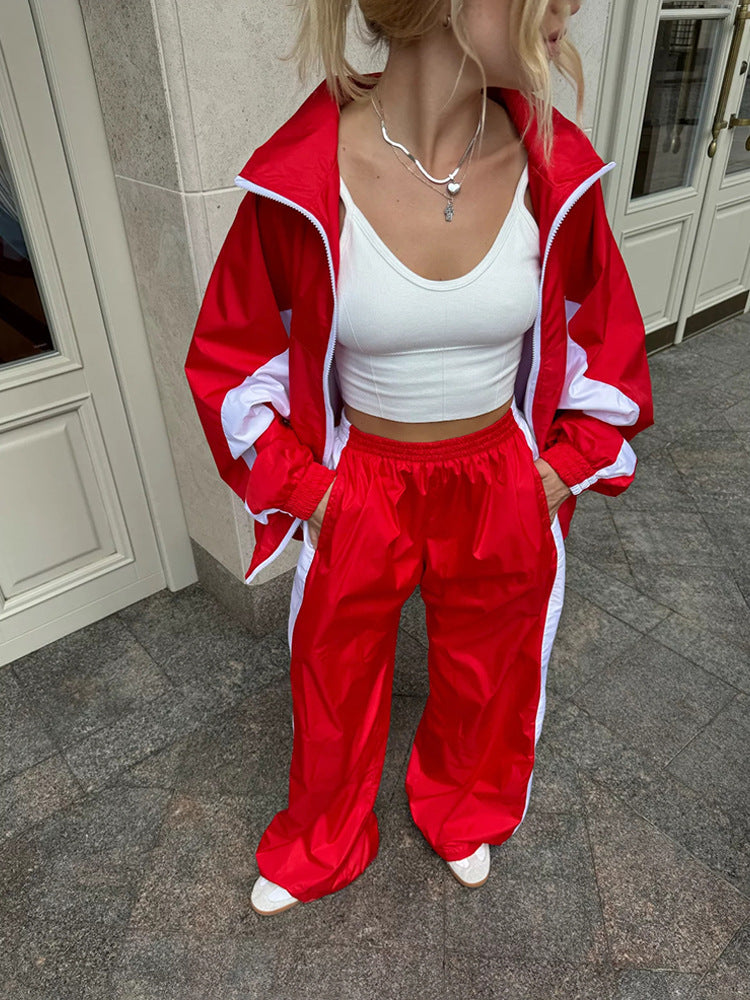 Close-up of a red windbreaker set with white panels and trim, worn with a white crop top and hands in the jacket pockets. 17