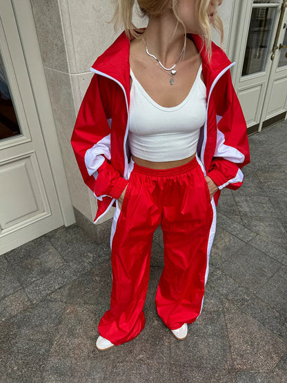 Close-up of a red windbreaker set with white panels and trim, worn with a white crop top and hands in the jacket pockets. 17