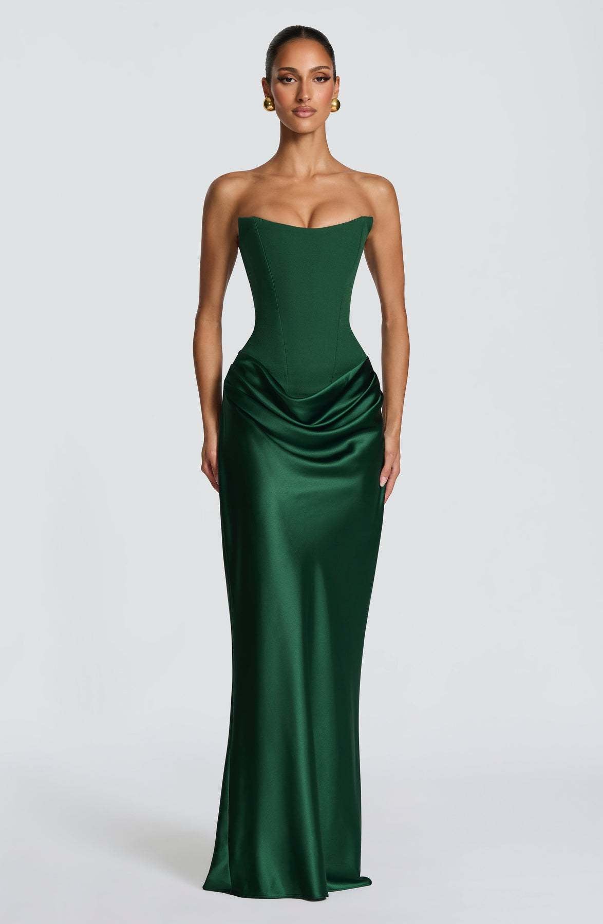 Model in strapless emerald green corset gown with draped satin skirt, front view on grey backdrop 1