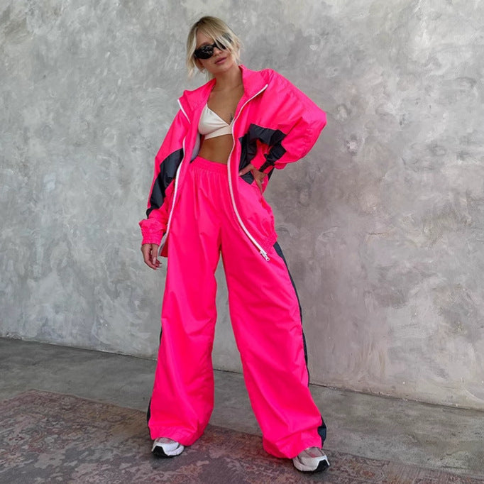 Model in a neon pink windbreaker set with dark grey panels and white zip, jacket open over a white bralette. 8
