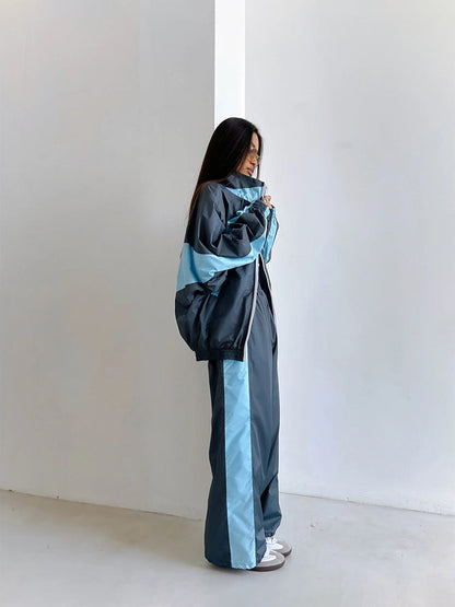 Side view of a model in a dark blue-grey windbreaker set with light blue chevron panels and a matching stripe down the trousers. 13