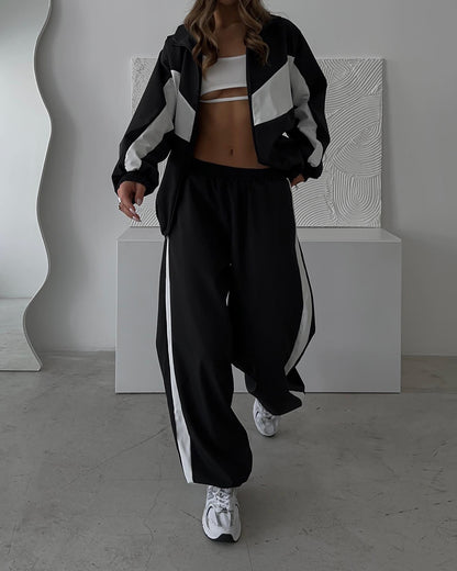 Model walking in the black set with white chevron panels on the zipped jacket and a white stripe down the wide trousers. 21