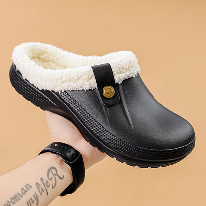Hand holding a black clog with cream fleece lining and buttoned strap against a beige backdrop 12