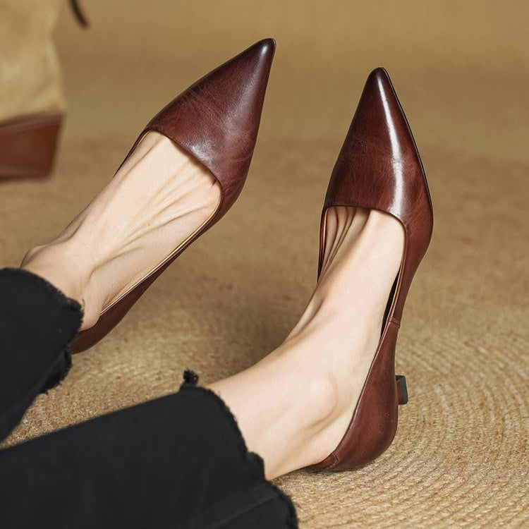 Worn pair of brown leather pointed-toe kitten heels, shown on feet against a woven rug 21