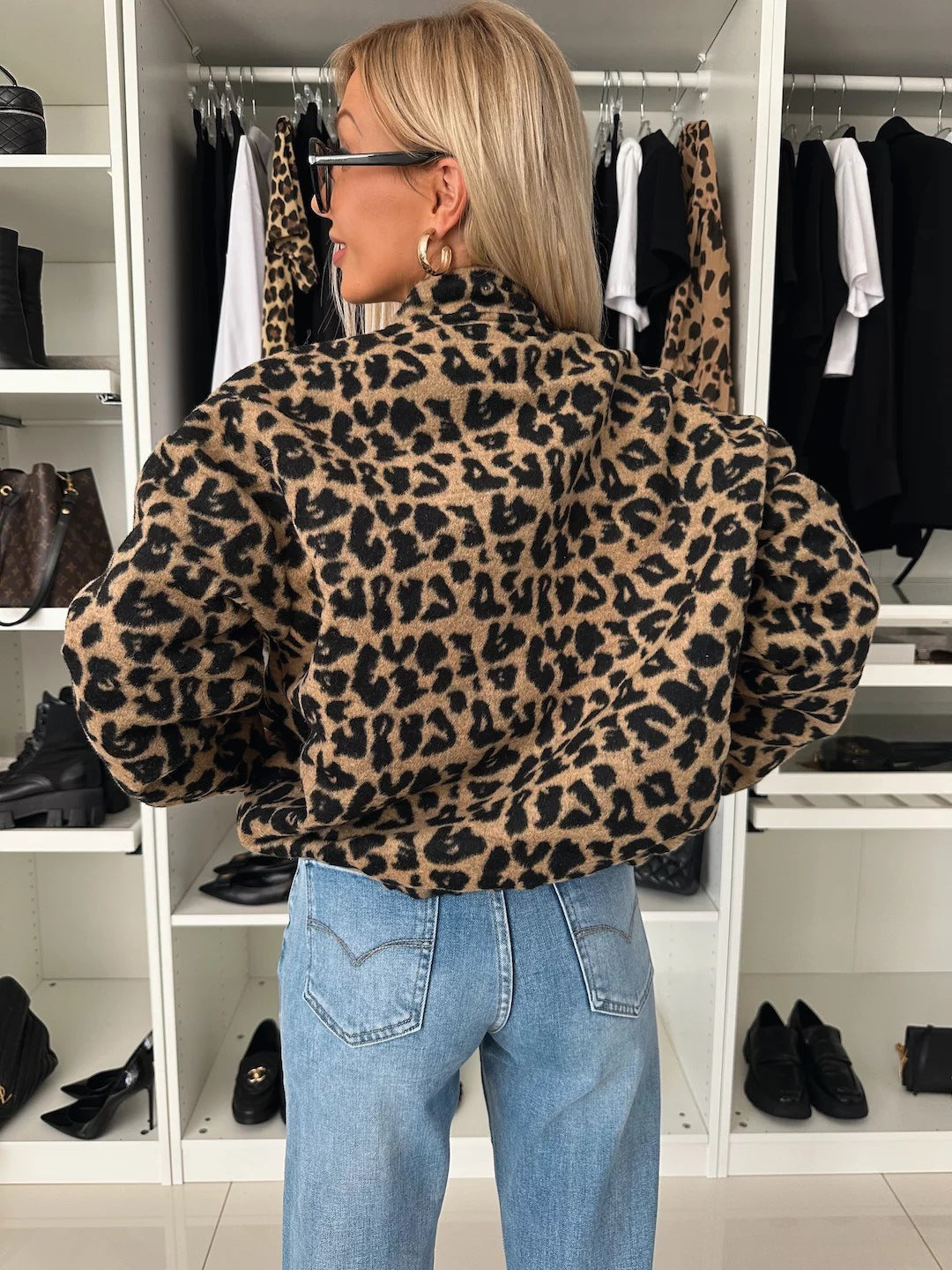 Back view of the leopard print bomber jacket on a model, showing the stand collar and full sleeves over blue jeans. 2