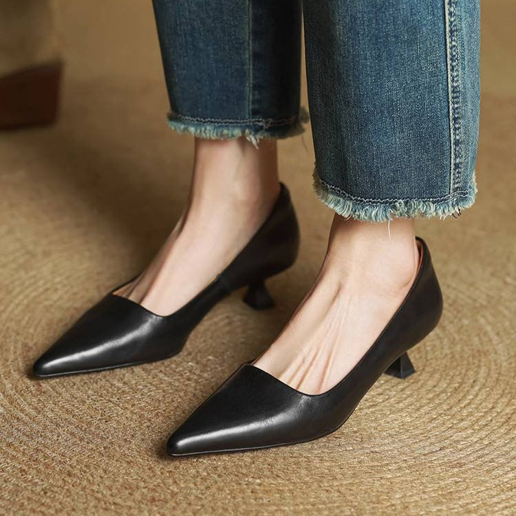 Black leather kitten heels worn with frayed-hem jeans, seen from the front on woven matting 13