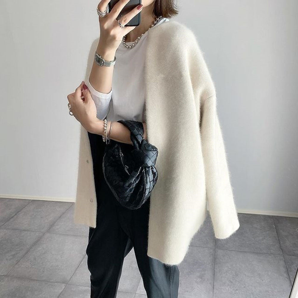 Three-quarter side view of the cream cardigan draped open over a white tee, black woven bag in hand 3