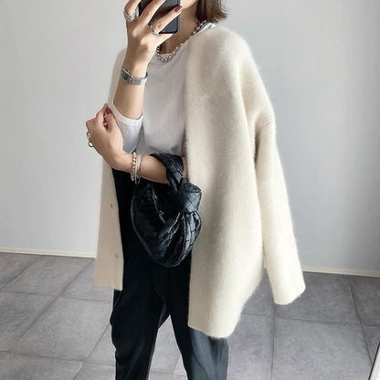 Three-quarter side view of the cream cardigan draped open over a white tee, black woven bag in hand 3