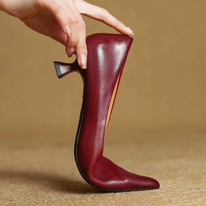 Hand holding a red leather pump upright on its toe to show its flexibility and slim heel 10