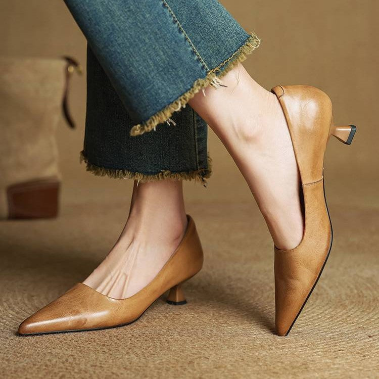 Tan pumps worn with raw-hem jeans, one foot raised to show the heel and pointed toe 3