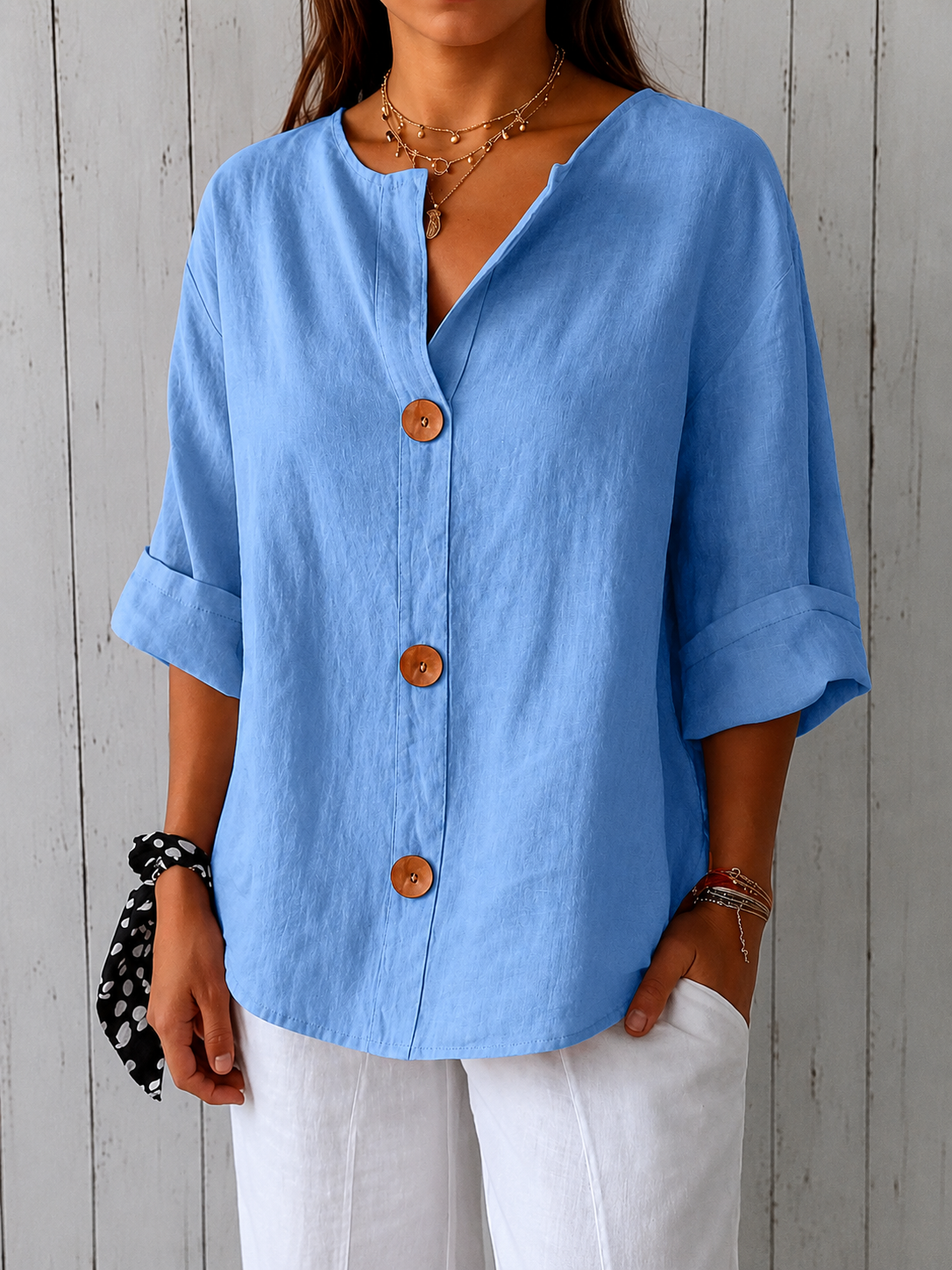 Front view of the light blue loose blouse on a model, showing the textured linen-look fabric, brown buttons, curved hem and cuffed sleeves. 13
