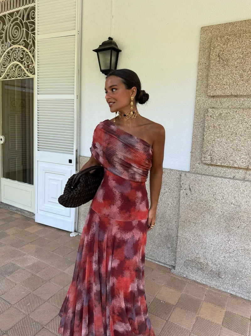 Model wearing red and purple tie-dye one-shoulder mesh dress with draped bodice, holding a woven bag 11