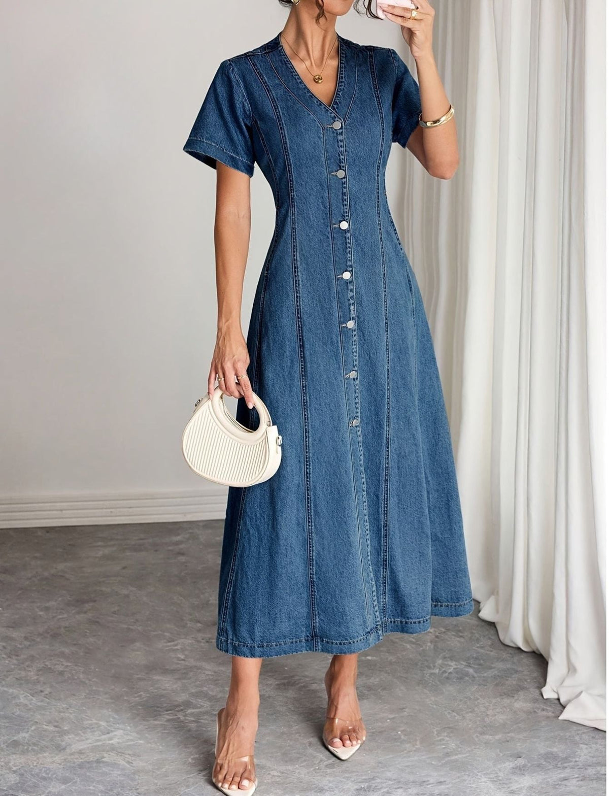 Model in the button-front denim midi dress holding a cream ribbed handbag, one hand raised 1