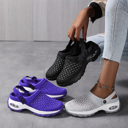 Three pairs of mesh clogs in purple, black and grey on a grey floor, one black pair held up by its heel straps. 4