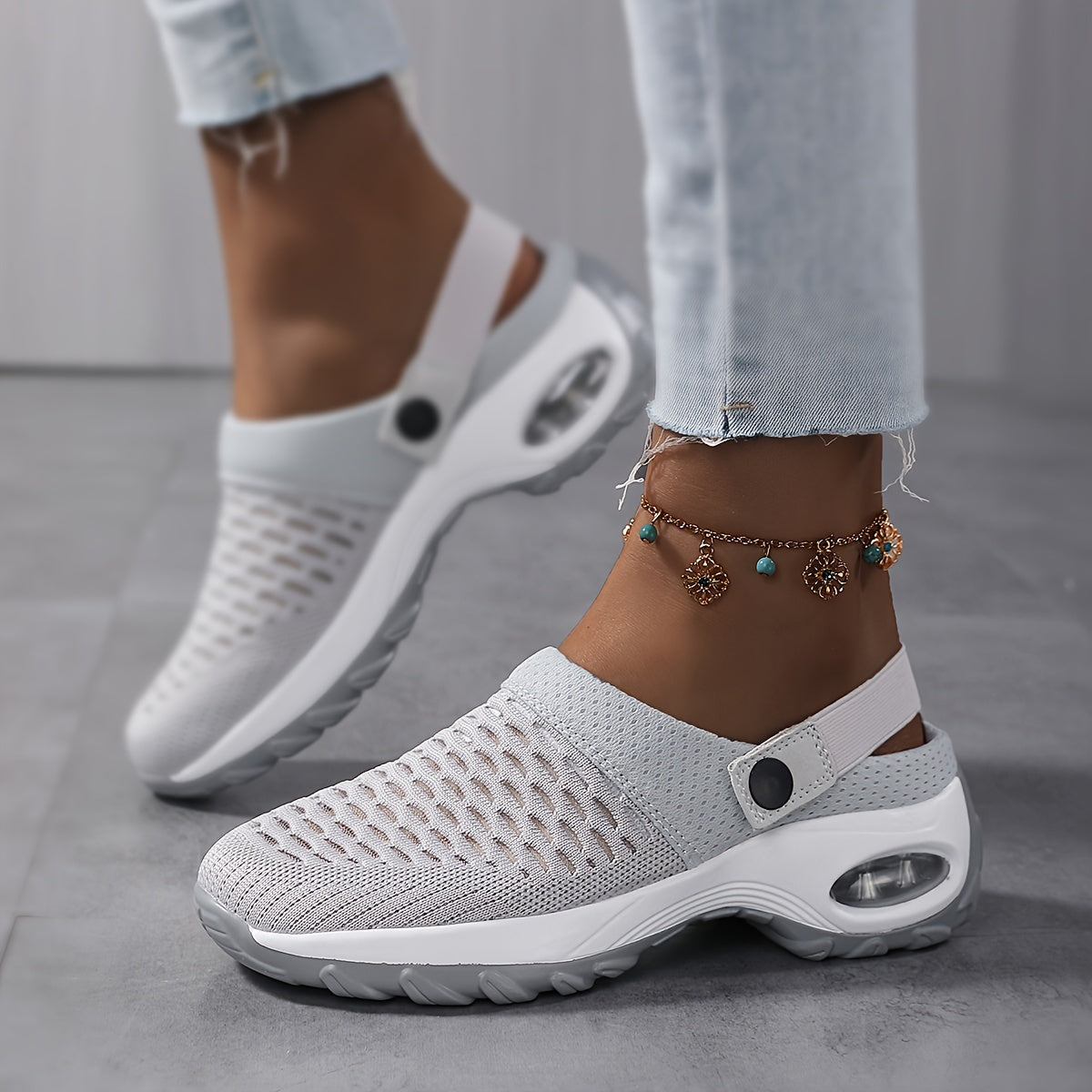 Model wearing light grey perforated mesh clogs with a white air-cushion sole and a charm anklet, walking on a grey floor. 5