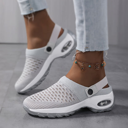 Model wearing light grey perforated mesh clogs with a white air-cushion sole and a charm anklet, walking on a grey floor. 5