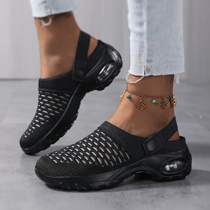 Model wearing black perforated mesh clogs with a tall black air-cushion sole and a heel strap, stepping on a grey floor. 7