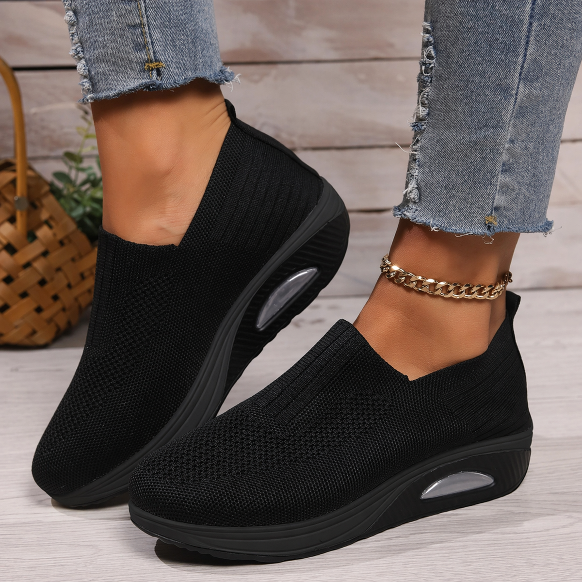 Black knit slip-on shoes with a thick black sole and visible air cushion, worn with frayed jeans and a gold ankle chain. 1