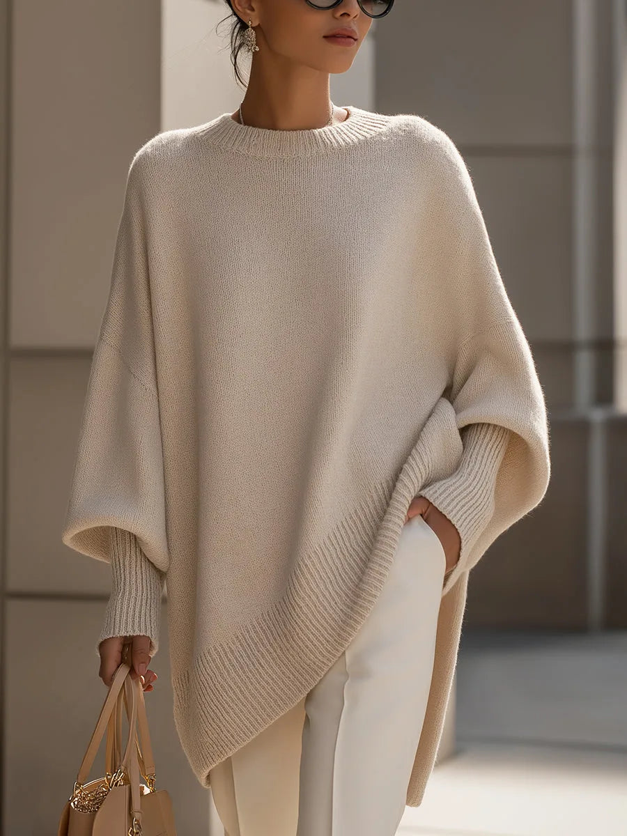 Model wearing the cream oversized jumper with white trousers, holding a beige handbag, hand in pocket 1