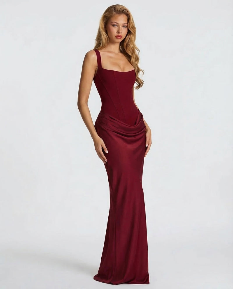 Deep red corset maxi dress worn at an angle by a model with wavy hair, showing the glossy draped skirt. 11