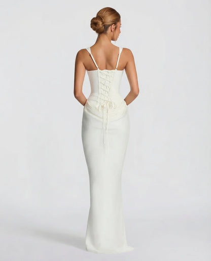Back view of the ivory dress showing thin adjustable straps, a lace-up corset back and long ties over the draped skirt. 6