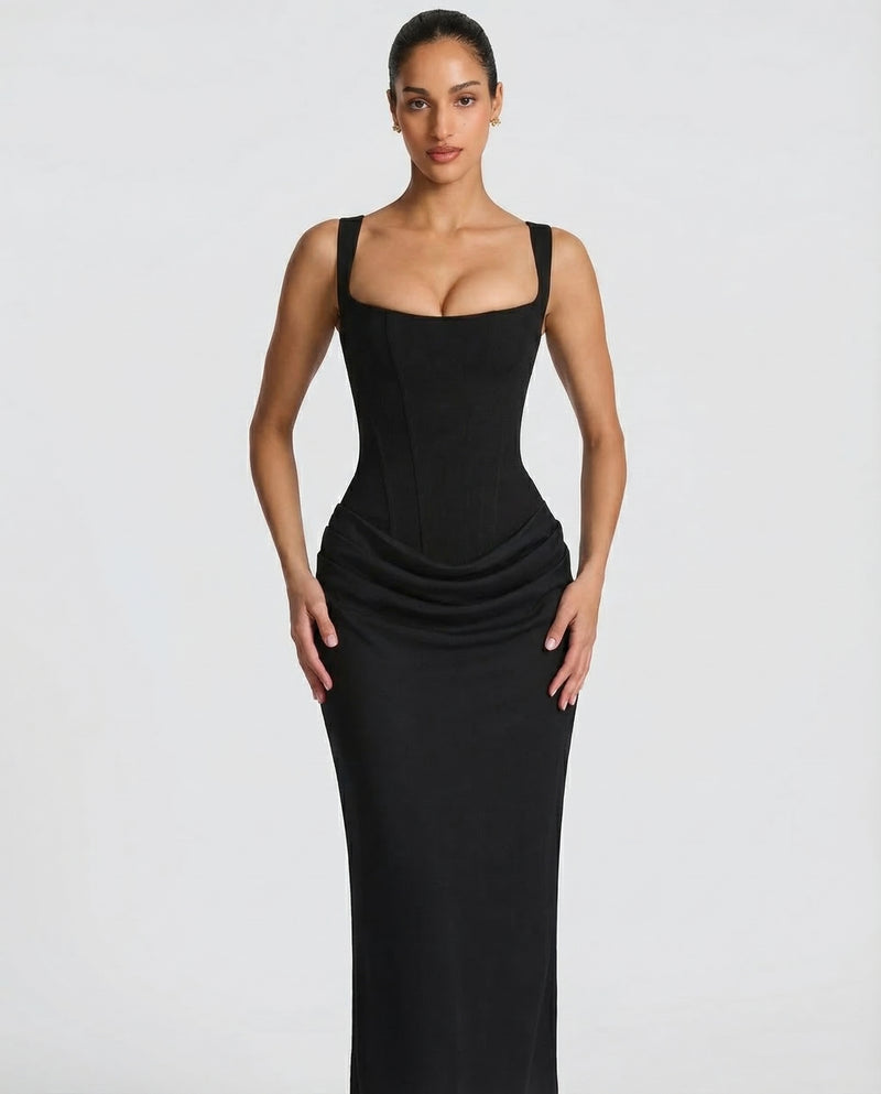 Close-up of the black dress's boned corset bodice, scooped square neckline and gathered drape at the hips, worn by a model. 3