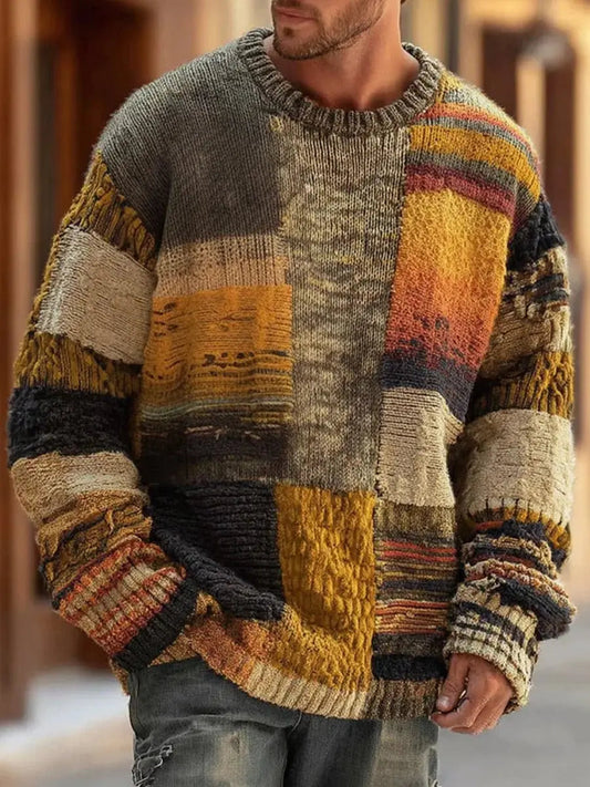 Man wearing the crew-neck sweater outdoors, front view showing mustard, grey, black and cream knitted patchwork panels 1