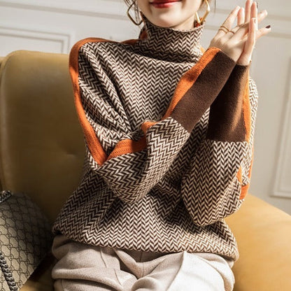 Model seated on a mustard armchair wears the brown herringbone jumper, showing the orange sleeve trim, brown cuffs and high neck. 4